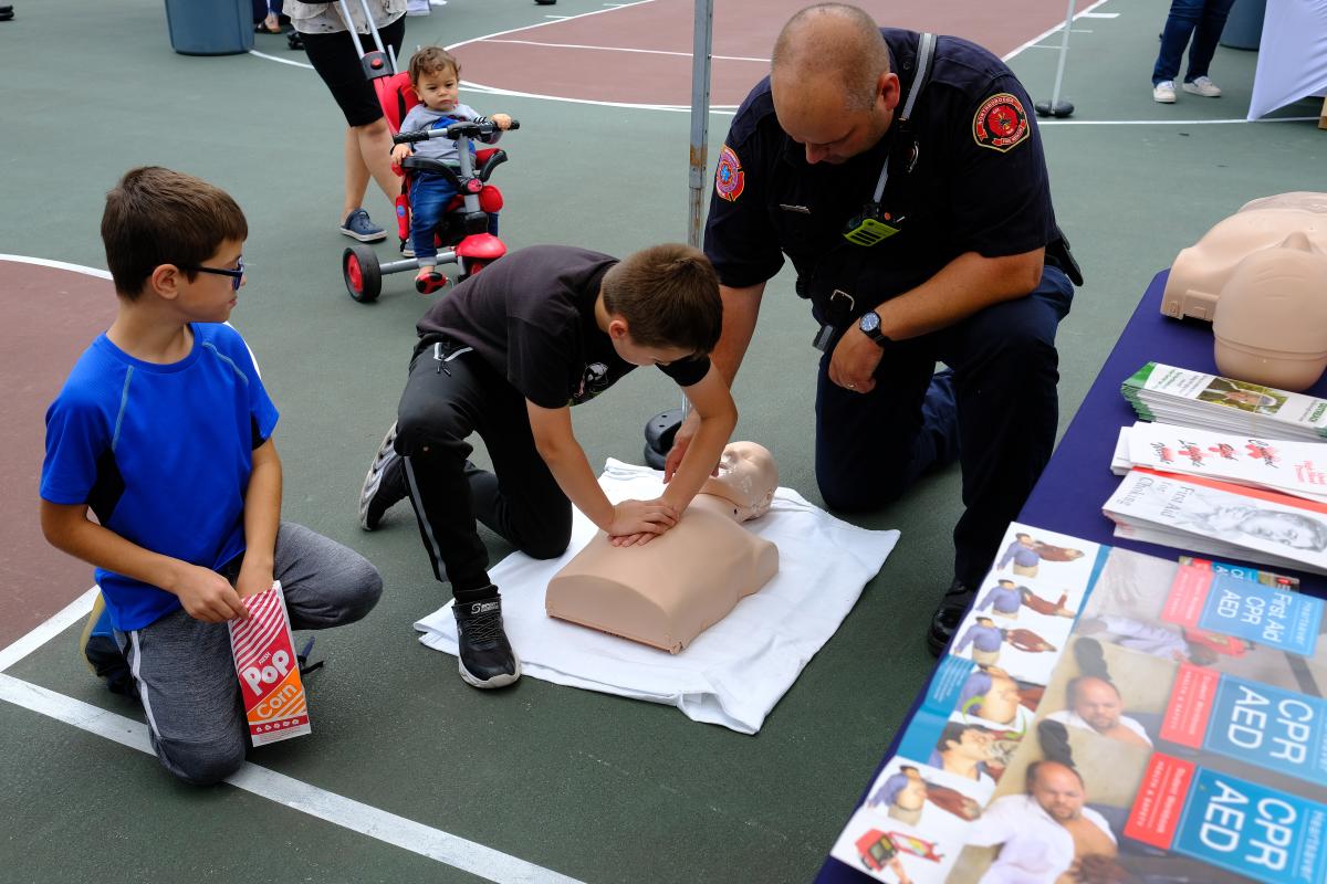 A firefighter helps a child to learn hands on CPR while another child looks on