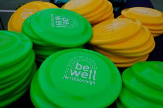 Stacks of green and yellow frisbees displaying the Be Well Northborough logo.
